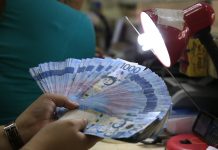A teller inspects one thousand pesos bills inside a money changer in Manila. REUTERS