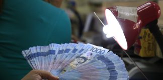 A teller inspects one thousand pesos bills inside a money changer in Manila. REUTERS