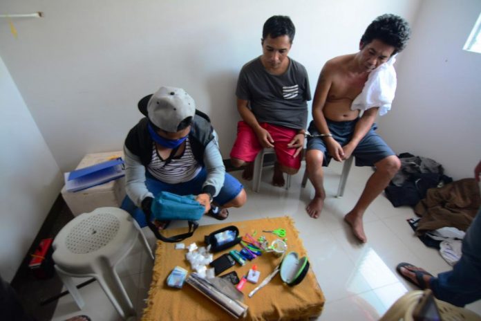 BUSTED DRUG SUSPECTS. Edwin Balinas of Santa Barbara, Iloilo and Janry Napat of Nabas, Aklan look on while an undercover policeman in civilian attire (left) checks the items recovered from them inside a house at a residential subdivision in Barangay Jibao-an, Pavia, Iloilo on Aug. 16, 2019. Sachets of suspected shabu valued at P810,000 were seized. IAN PAUL CORDERO/PN