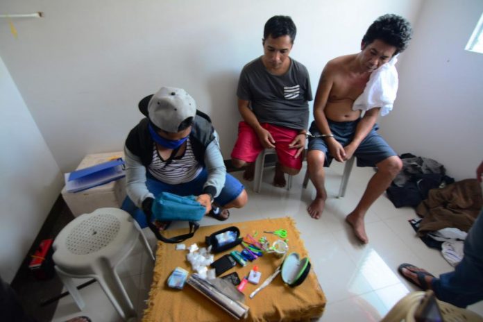 Edwin Balinas of Santa Barbara, Iloilo and Janry Napat of Nabas, Aklan Pavia Drugs BUSTED DRUG SUSPECTS. Edwin Balinas of Santa Barbara, Iloilo and Janry Napat of Nabas, Aklan look on while an undercover policeman in civilian attire (left) checks the items recovered from them inside a house at a residential subdivision in Barangay Jibao-an, Pavia, Iloilo on Aug. 16, 2019. Sachets of suspected shabu valued at P810,000 were seized. IAN PAUL CORDERO/PN