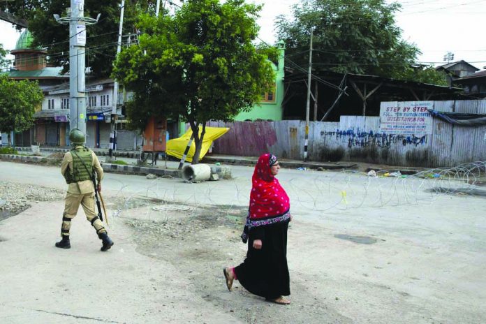 A Kashmiri woman walks past an Indian paramilitary soldier who prepares to block a road with barbed wires during security lockdown in Srinagar, Indian controlled Kashmir, Sunday, Aug. 18, 2019. AP