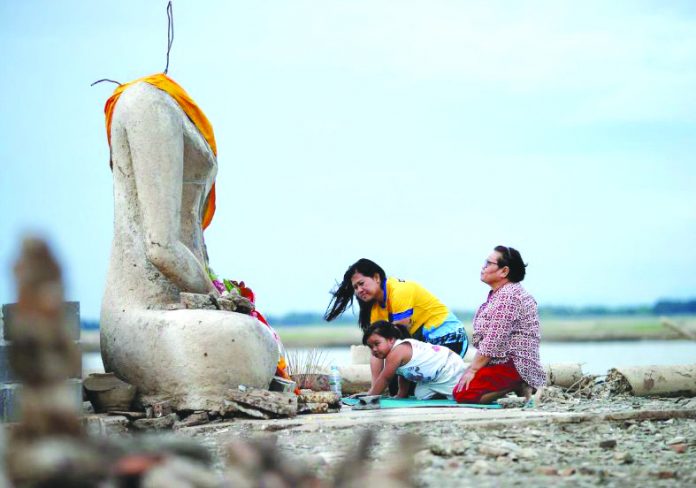 Thailand Temple drought A family prays near the ruins of a headless Buddha statue, which has resurfaced in a dried-up dam due to drought, in Lopburi, Thailand August 1, 2019. REUTERS