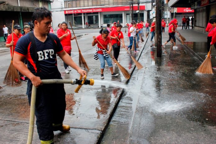 An officer of the Bureau of Fire Protection flushes water on the road while members of the city enforcement units sweep the area in Bacolod City on Monday. BACOLOD CITY PIO
