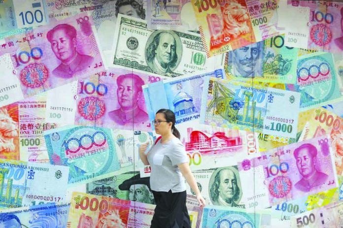 China In this Aug. 6, 2019, file photo, a woman walks by a money exchange shop decorated with different countries currency banknotes at Central, a business district in Hong Kong. AP