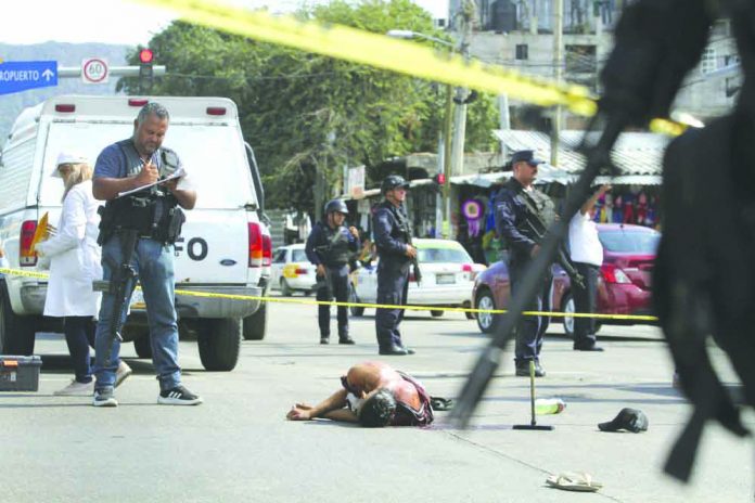 In this June 2, 2019 file photo, the body of a bloodied man lies in the middle of a street where police and forensic workers secure the crime scene in Acapulco, Mexico.