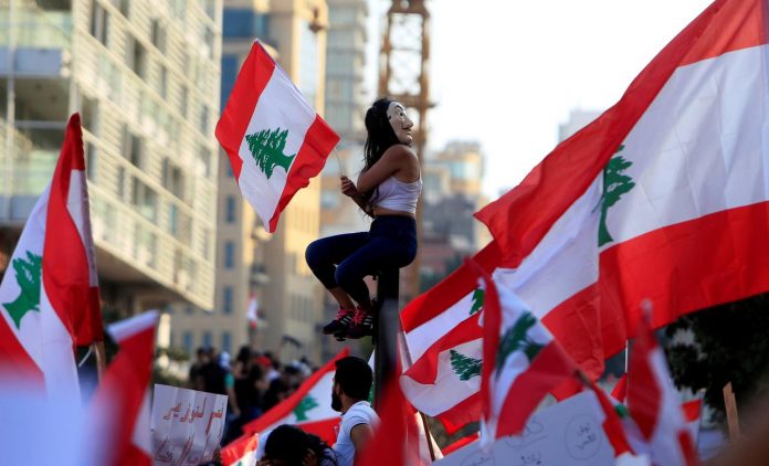 A demonstrator sits on a pole while carrying a national flag during an anti-government protest in downtown Beirut, Lebanon on Oct. 20. REUTERS/ALI HASHISHO