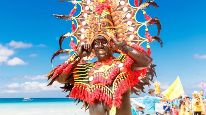 Man in a colorful headdress during the Ati-Atihan celebration in Boracay Island, Malay, Aklan. The Kalibo Santo Niño Ati-Atihan Management Council Incorporated is eyeing to revive the classic 1980s favorite – the snake dancing tradition in the capital town. FROLOVA_ELENA/ SHUTTERSTOCK