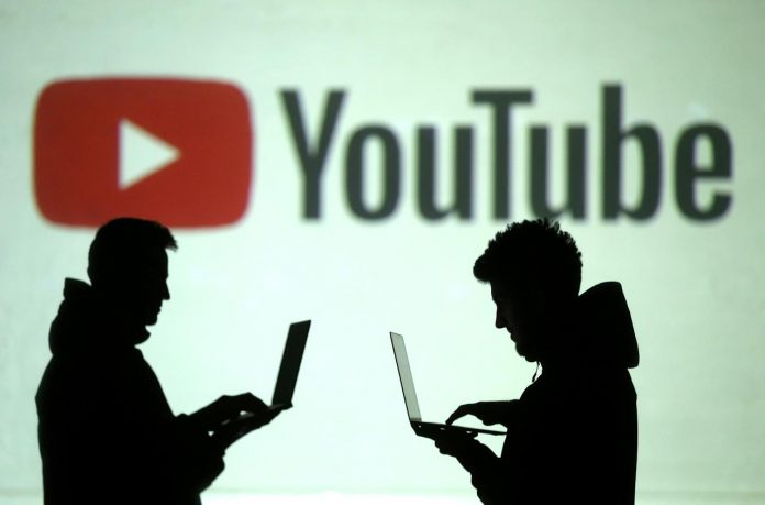 Silhouettes of users are seen next to a screen projection of the Youtube logo. YouTube broadened its anti-harassment policies to include a ban on “implied” threats and insults based on race, gender identity or sexual orientation. REUTERS