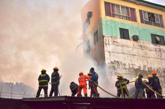 Iloilo City Fire TO THE RESCUE. Firefighters of the Bureau of Fire Protection in Iloilo City and from volunteer groups position themselves atop this roof to spray with water the houses burning behind a tall wall in Barangay Gloria, Iloilo City on Sunday afternoon, Feb. 16, 2020. This is the second fire to hit the city yesterday. In the morning, fire struck Barangay Concepcion also in the City Proper. IAN PAUL CORDERO/PN