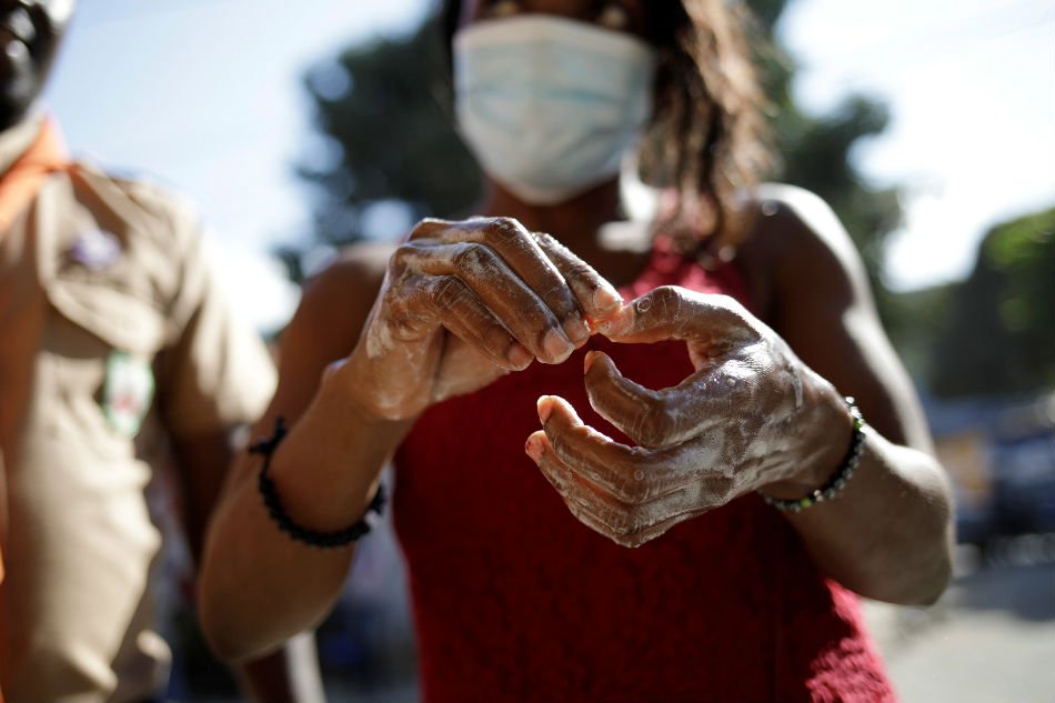 A woman wearing a protective mask washes her hands at a hand-washing station set up by Haitian Boy and Girl Scouts to prevent the spread of coronavirus disease (COVID-19) in Port-au-Prince, Haiti Mar. 13, 2020. REUTERS