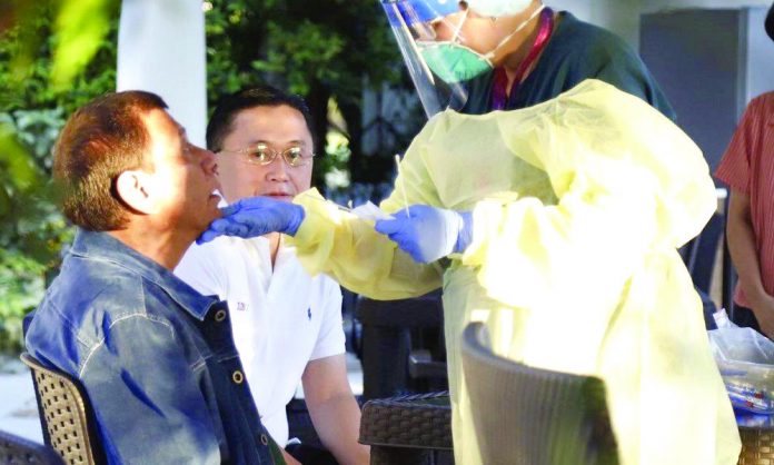 Duterte A medical worker does a mouth swab on President Rodrigo Duterte Thursday as close ally Sen. Christopher “Bong” Go looks on. PTV