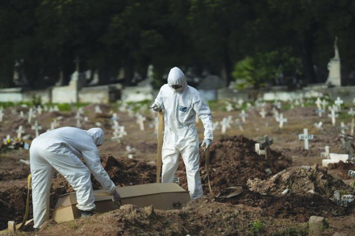 Cemetery workers in protective clothing maneuver the coffin of 57-year-old Paulo Jose da Silva, who died from the new coronavirus