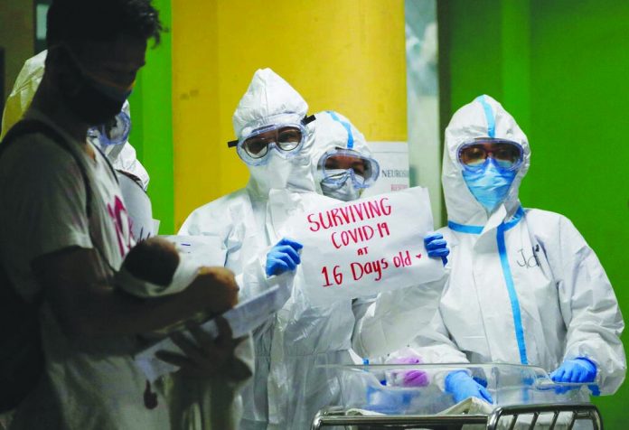 Health workers wearing protective suits hold a sign beside a 16-day-old baby who recovered from COVID-19 is held by his father at the National Children’s Hospital in Quezon city, Metro Manila.