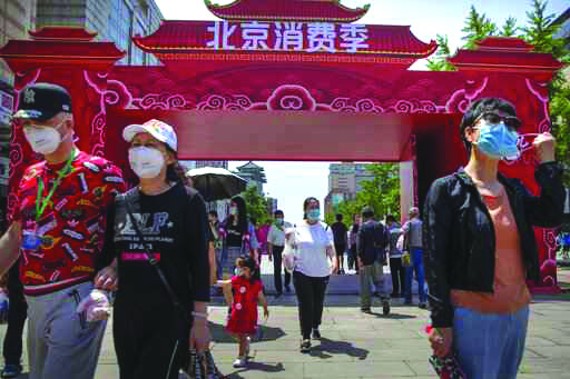 People wearing face masks to protect against the new coronavirus walk at a government event aiming to stimulate consumer demand and consumption in Beijing, Saturday, June 6, 2020.