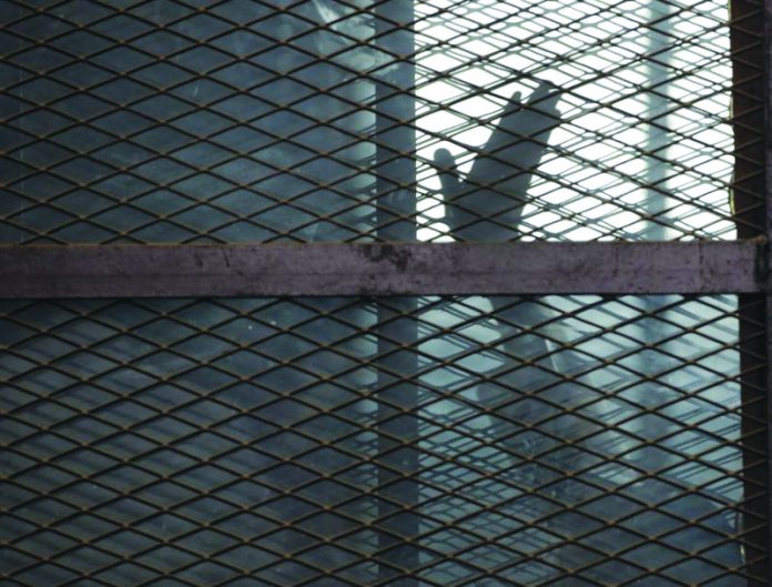 In this Aug. 22, 2015 file photo, a Muslim Brotherhood member waves his hand In this Aug. 22, 2015 file photo, a Muslim Brotherhood member waves his hand from a defendants cage in a courtroom in Torah prison, southern Cairo, Egypt. AP