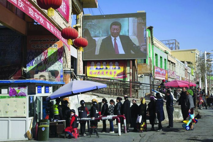 In this Nov. 3, 2017, file photo, residents line up at a security checkpoint In this Nov. 3, 2017, file photo, residents line up at a security checkpoint into the Hotan Bazaar where a screen shows Chinese President Xi Jinping in Hotan in western China's Xinjiang region. AP PHOTO/NG HAN GUAN