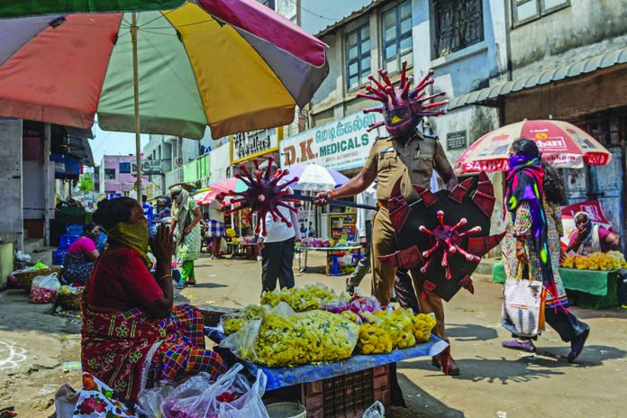 INDIA-HEALTH-VIRUS A policeman (right) wearing a coronavirus-themed outfit composed of helmet, mace and shield, gestures towards a vendor at a market to raise awareness about social distancing, during a government-imposed nationwide lockdown as a preventive measure against the COVID-19, in Chennai on April 2, 2020. AFP