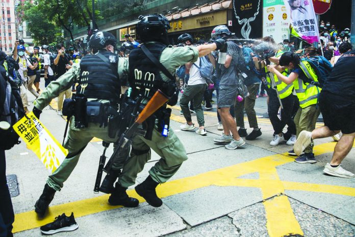 Riot police (left) deploy pepper spray toward journalists (right) as protesters gathered for a rally against a new national security law in Hong Kong on July 1, 2020. AFP