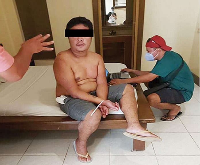 Romeo Timeex Bat-og II sits handcuffed while authorities inspect his laptop during an entrapment operation in a motel in La Paz, Iloilo City on Dec. 29. He was accused of blackmailing a 16-year-old girl in exchange for not posting her nude photos online. PRO-6