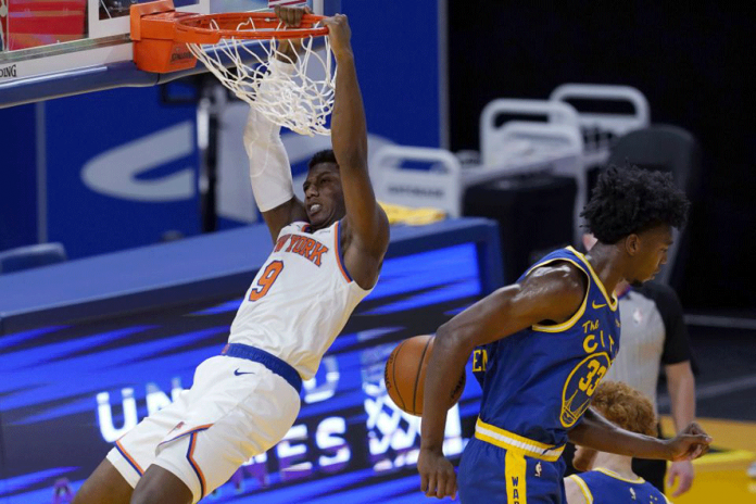 nba New York Knicks guard RJ Barrett hangs from the rim after dunking next to Golden State Warriors center James Wiseman during the second half of an NBA basketball game on Jan. 21, 2021. JEFF CHIU/AP PHOTO