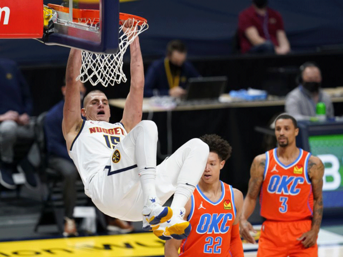 nba Denver Nuggets center Nikola Jokić hangs from the rim after dunking the ball for a basket against Oklahoma City Thunder forward Isaiah Roby and guard George Hill in the first half of an NBA basketball game on Jan. 19, 2021. David Zalubowski/AP Photo