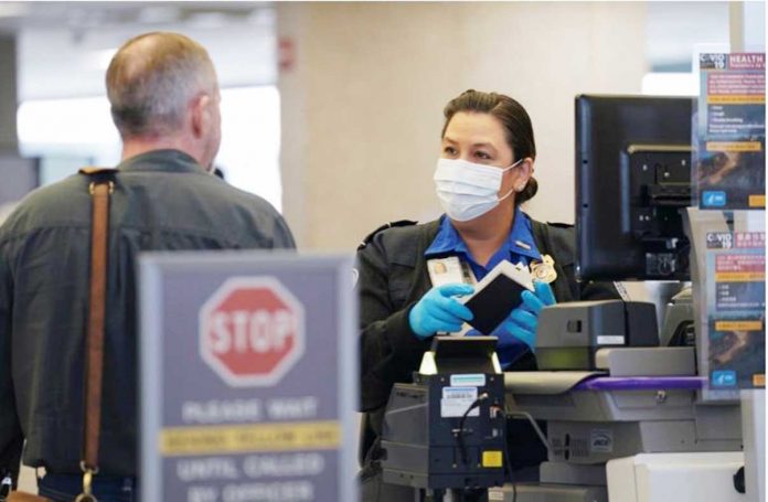 An officer wearing a face mask clears a departing passenger at Dulles International Airport. KEVIN LAMARQUE/REUTERS An officer wearing a face mask clears a departing passenger at Dulles International Airport. KEVIN LAMARQUE/REUTERS