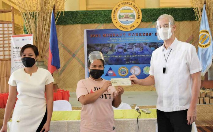 displace-ofws A displaced OFW receives a P20,000 check as financial assistance from Negros Occidental’s Governor Eugenio Jose Lacson (right) in the presence of OWWA-Western Visayas officer-in-charge Rizza Joy Moldes (left) during the Migrant Workers Day program on Monday. PIO NEGROS OCCIDENTAL