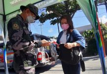 An authorized person outside residence (APOR) presents her travel pass to a police officer at a checkpoint in Barangay Mohon, Arevalo, Iloilo City.