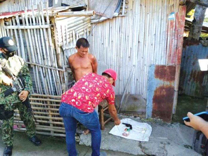 Gunrunning suspect Johny Helario (shirtless) looks on as police operatives check the items recovered from him in Barangay Tanque, Roxas City.