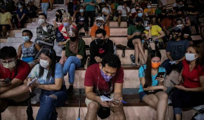 news-vax People waiting for their turn at a vaccination site in Manila use their phones to while away time. REUTERS