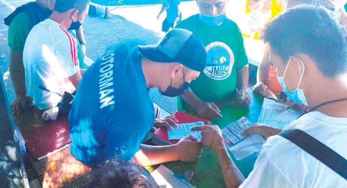 front-pic AUTHENTIC OR FAKE? An inspector at the Parola wharf in Iloilo City scrutinizes the COVID-19 vaccination card of a man who intends to travel to nearby Guimaras Island. Aside from the vaccination card, the man is also required to present a valid identification card and an outbound pass. PN PHOTO