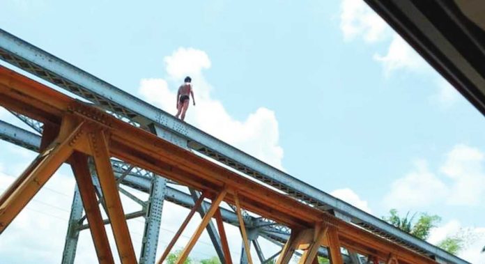 Robbery suspect Fernando Camporaso Jr. climbed onto trusses of the Caliban bridge in Barangay Caliban, Murcia, Negros Occidental on Sunday, May 14, after carting away P7,800 in cash from a lending collector. APRIL MAHUSAY PHOTO