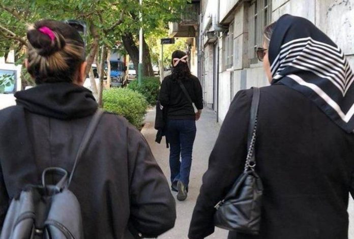 iran Two women walk down a street, facing away from the camera – one is wearing a headscarf and one is not. Some women in Iran are choosing not to cover their hair as part of ongoing protests. HANDOUT