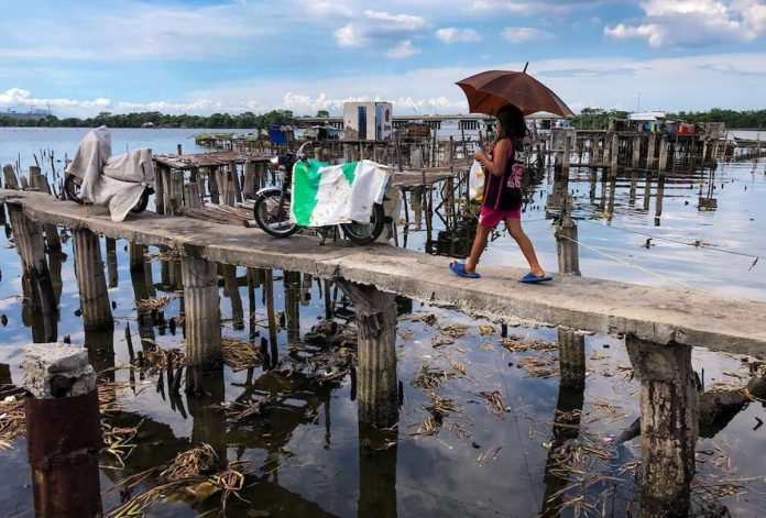 poverty_in_asia_resized A woman walks on a narrow bridge towards huts made out of light materials at a fishing community in Bacoor, Cavite on October 30, 2020. GEORGE CALVELO, ABS-CBN NEWS PHOTO