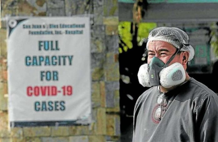 A health worker stands beside an advisory that reads “Full Capacity for COVID-19 cases” posted at a hospital in Pasay City at the height of the pandemic in 2021. File photo by RICHARD A. REYES / Philippine Daily Inquirer