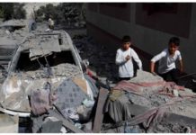 Ceasefire in Gaza by the start of Ramadan? Two boys are seen standing next to a car that is heavily damaged and covered in debris in Gaza. In the foreground is what appears to be the rubble of a collapsed building. REUTERS