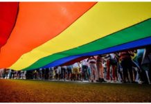 A camera shot taken from beneath a large LGBT rainbow flag shows people's legs standing to the right of the flag during a rally. AFP