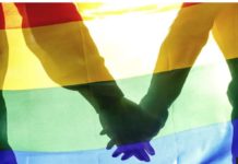 Two people hold hands behind a rainbow flag. In Iran, LGBT people have faced persecution for many years, with rights groups detailing cases of rape, torture and murder. GETTY IMAGES
