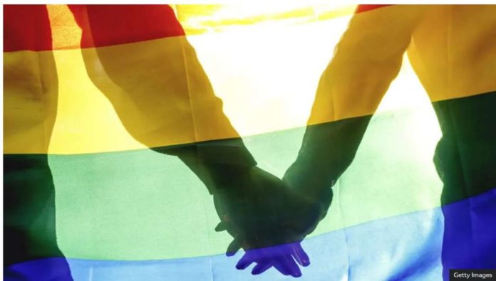 Two people hold hands behind a rainbow flag. In Iran, LGBT people have faced persecution for many years, with rights groups detailing cases of rape, torture and murder. GETTY IMAGES