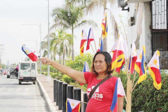 mai_flag_vendors_-_Loredil_Ariola Vendors Jike Nava, Loredil Ariola, and Jerry Potato sell miniature Philippine flags on the bustling streets of Iloilo City, embodying the patriotic spirit of Independence Day. Of course, they wish of brisk sales. They say independence should also be synonymous with economic freedom and opportunities for all Filipinos. AJ PALCULLO/PN