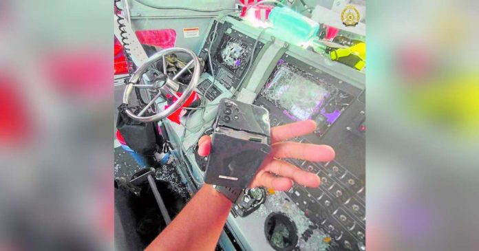 AFP_superimposed A Philippine Navy sailor shows a cell phone that was allegedly cracked open by a China Coast Guard member against the backdrop of smashed navigational and communication equipment of a resupply boat at Ayungin (Second Thomas) Shoal during the June 17 attack by the Chinese who wielded knives and axes while threatening the Filipinos who tried to deliver essential provisions for troops on the BRP Sierra Madre which is grounded there. PHOTO FROM ARMED FORCES OF THE PHILIPPINES