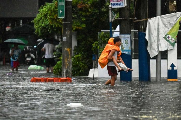 DOH_resized A man piggybacks a person along a flooded street in Manila on July 24, 2024 amid heavy rains. AFP