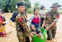 Floods, mudslides kill more than 200 in Myanmar Two soldiers carry an elderly woman in a bucket as they wade through knee-deep muddy water. Behind them several other civilians, carrying children, make their way through the flooding as well. GETTY IMAGES