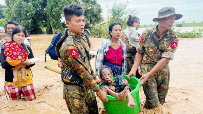 Myanmar_1_resized Two soldiers carry an elderly woman in a bucket as they wade through knee-deep muddy water. Behind them several other civilians, carrying children, make their way through the flooding as well. GETTY IMAGES