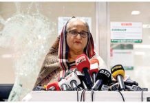 Bangladesh issues arrest warrant for ex-leader Hasina Sheikh Hasina, wearing a headscarf and glasses, speaks to reporters in front several microphones and with smashed glass behind her at a vandaliZed metro station in Mirpur on July 25, 2024. GETTY IMAGES
