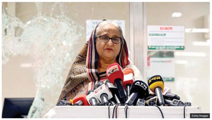 Bangladesh_1_resized Sheikh Hasina, wearing a headscarf and glasses, speaks to reporters in front several microphones and with smashed glass behind her at a vandaliZed metro station in Mirpur on July 25, 2024. GETTY IMAGES