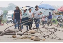 Bolivian ex-leader’s looming arrest warrant triggers protests A woman wearing a straw hat and a small group of other people walk on a road strewn with rocks and branches. The branches are blocking the road and are part of a blockade installed by followers of former president Evo Morales in Bolivia. EPA