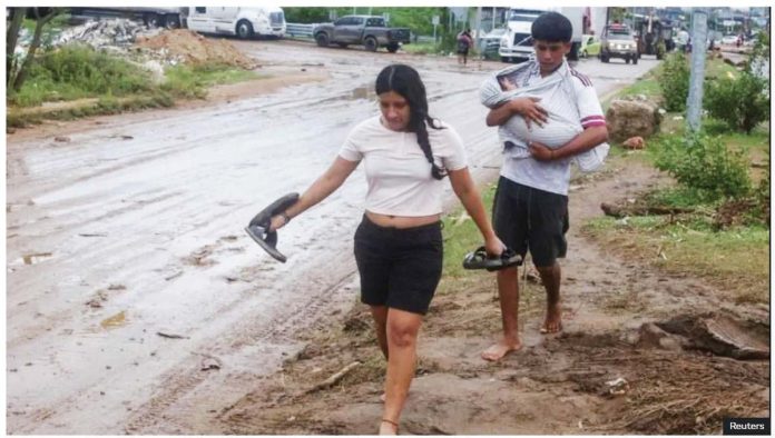Mexico_1_resized A woman and a man holding a baby walk barefoot on a muddy street in Acapulco, Guerrero, Mexico. Many families had to seek safety in shelters after their homes were flooded. REUTERS