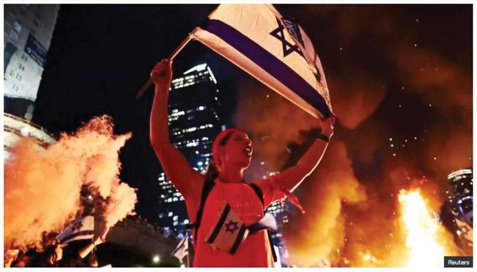 Israel-1 A person holds an Israeli flag as people demonstrate after Israeli Prime Minister Benjamin Netanyahu sacked his defense minister, Yoav Gallant, citing lack of trust, in Tel Aviv, Israel. REUTERS