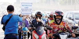 A motorcycle rider flashes the thumbs-up sign to a traffic constable carrying a placard that reads “Motorcycle Lane Exclusive for Motorcycle” along Commonwealth Avenue in Quezon City. PNA